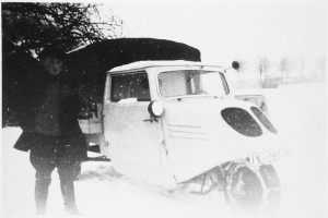 Ein Mann steht bei Schnee vor einem dreirädrigen motorisierten Fahrzeug, welches mit Schneeketten ausgestattet ist.