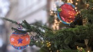 Detail eines Weihnachtsbaums in einem Straßenzug, am Tannenzweig zwei bunte Papieranhänger in Form von Weihnachtskugeln und eine Lichterkette
